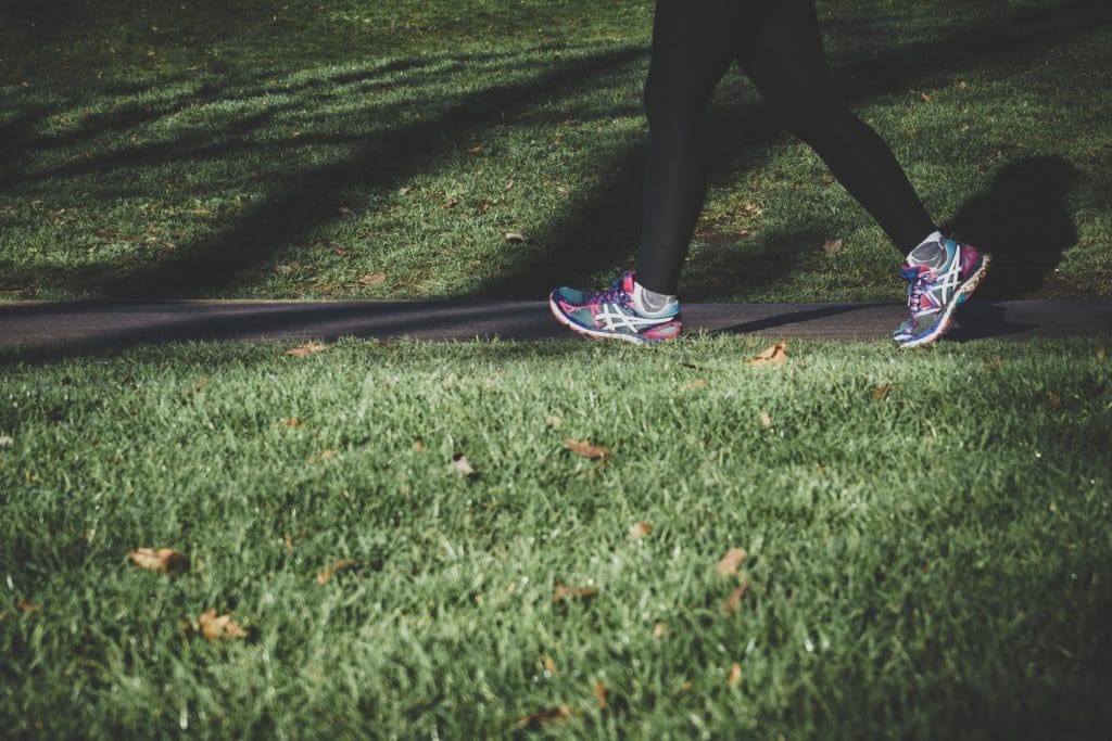 Plan serrer sur des pieds chaussés de baskets colorées en pleine marche sportive, sur un chemin bordé d'herbe courte.