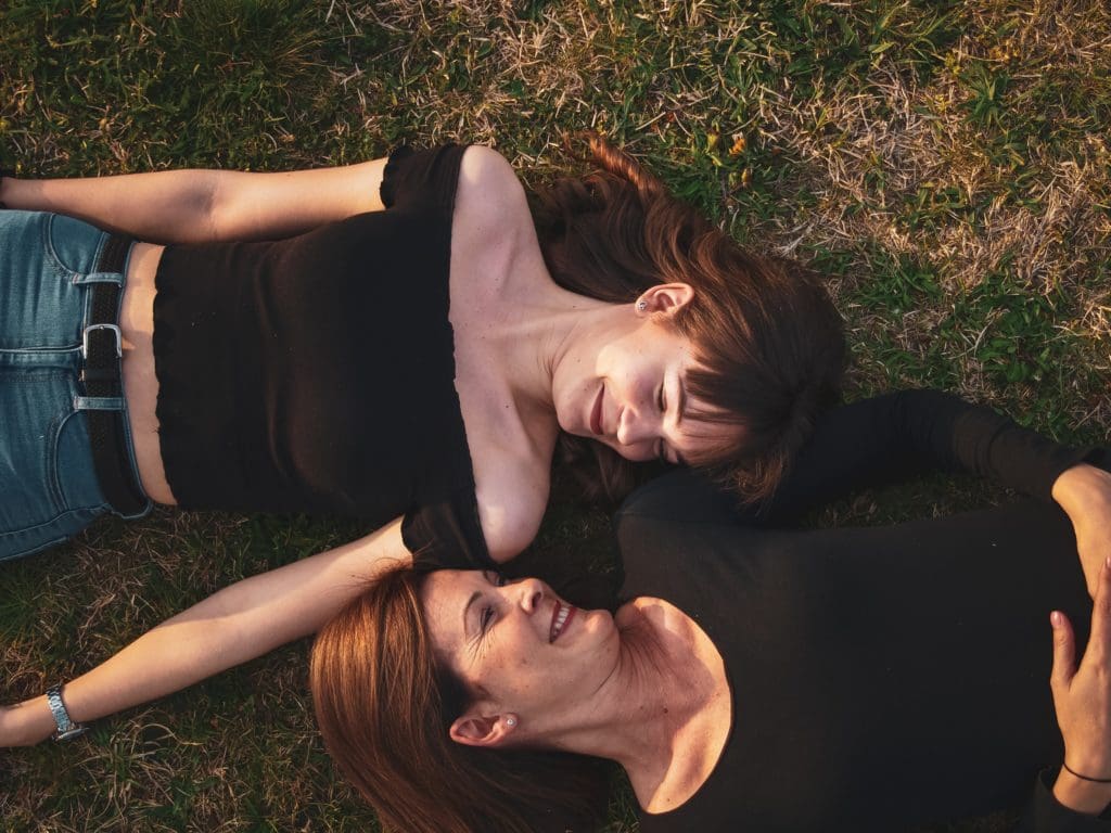 Deux femmes qui se regardent avec le sourire, allongées dans l'herbe.