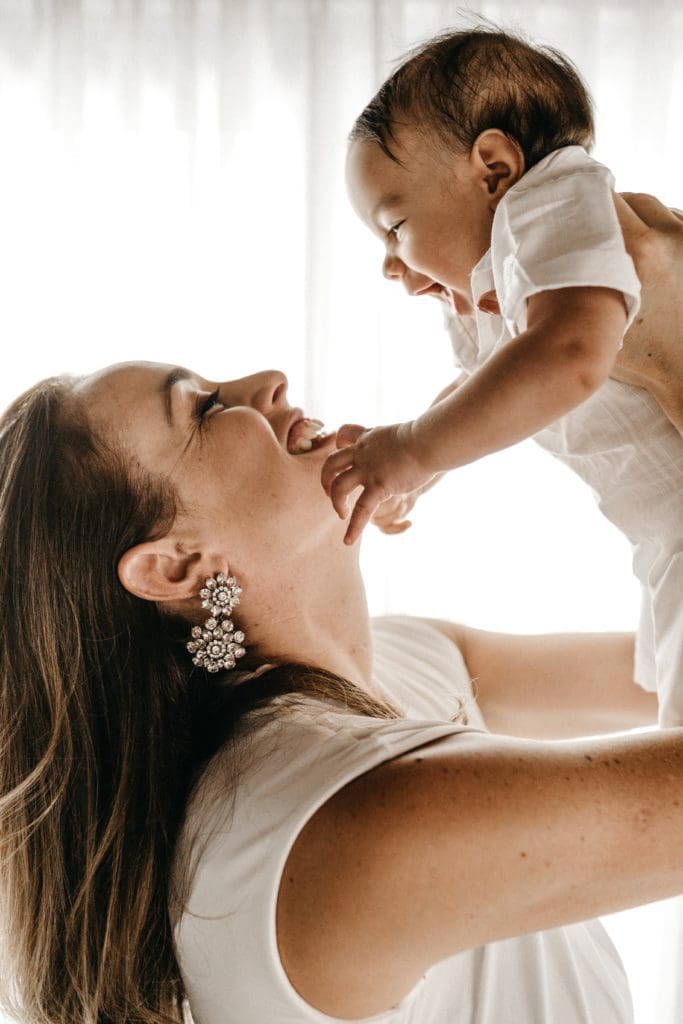 Photo de profil d'une femme tenant son bébé au dessus de son visage. Les deux sont souriants et semblent heureux