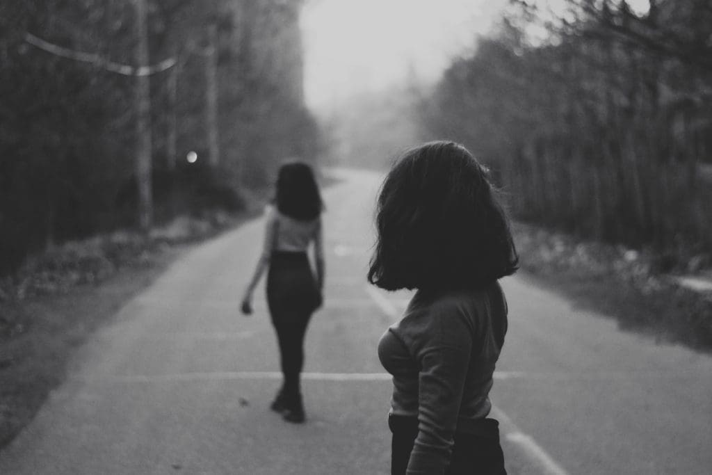 Photo noir et blanc. Une femme en deuxième plan s'éloigne de dos. Une femme en premier plan observe la premère, dos au lecteur.