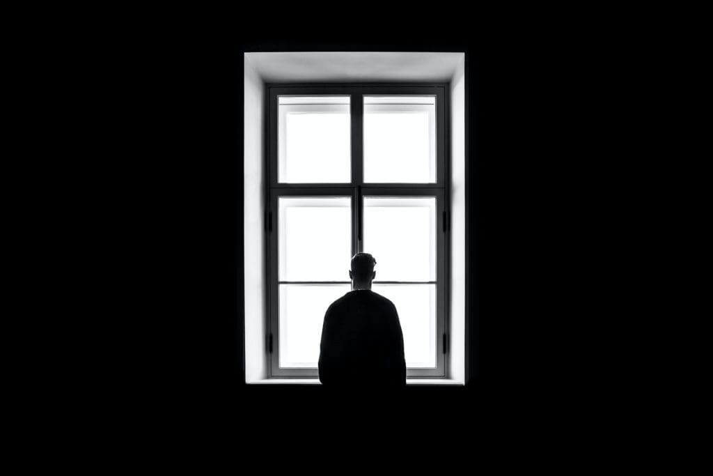 Homme de dos face à une fenêtre, image en noir et blanc