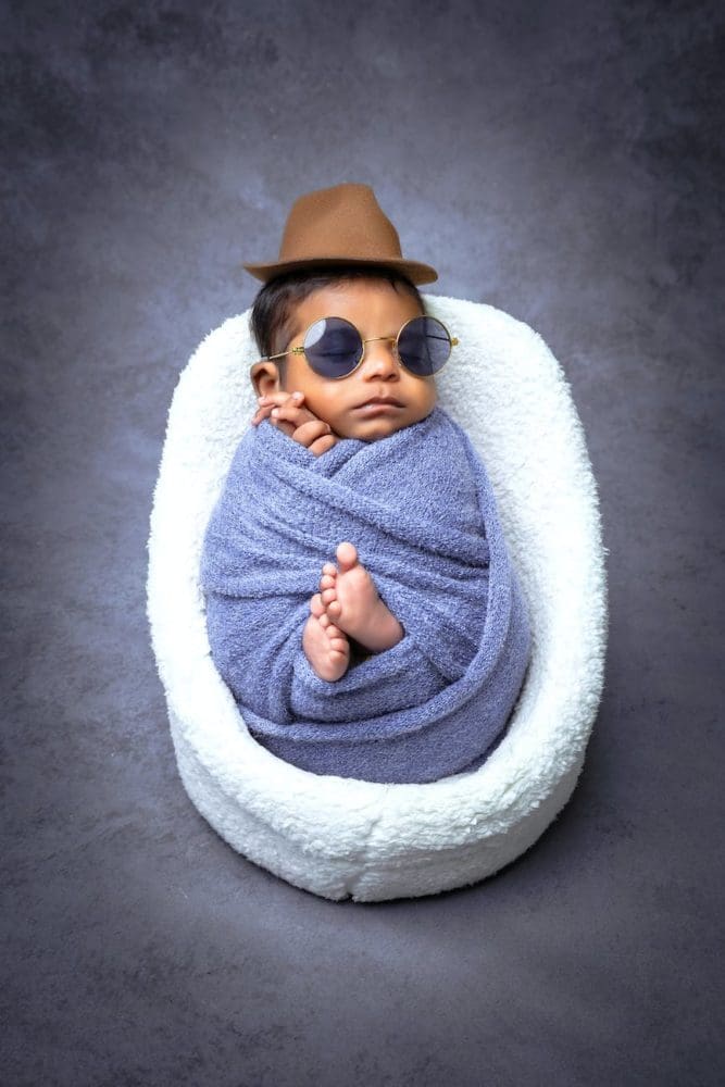 bébé métisse emmailloté, avec un petit fédora et des lunettes de soleil