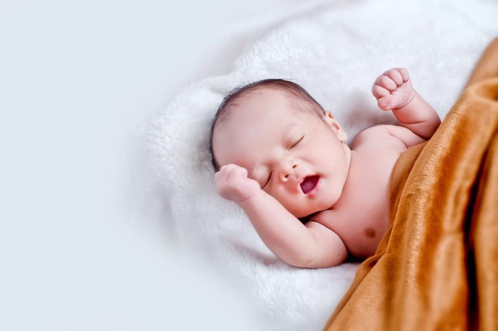 nouveau né qui s'étire, couché sur un linge, couvert d'une couverture beige