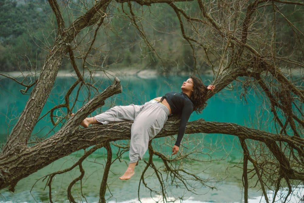 woman lying on a tree branch by a body of water