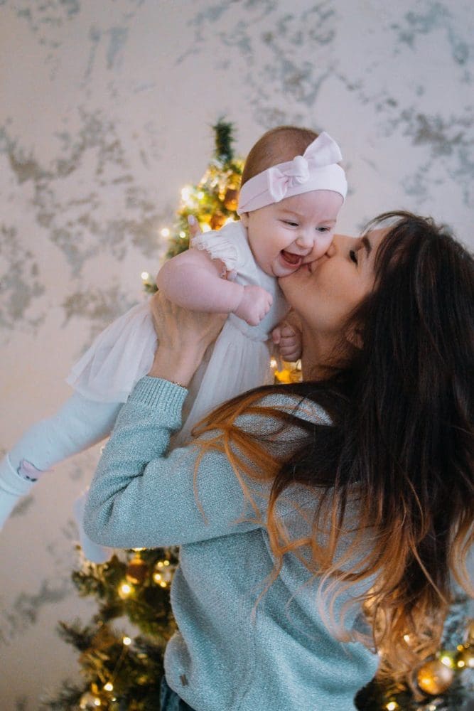 mother kissing child near christmas tree at home