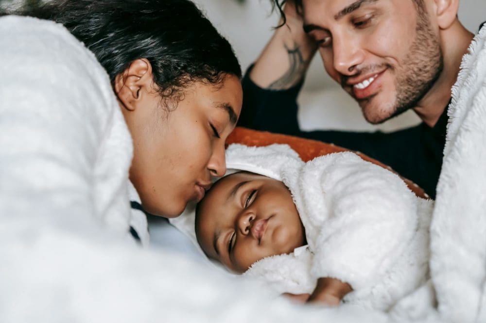 cheerful young multiethnic parents admiring sleeping baby on bed